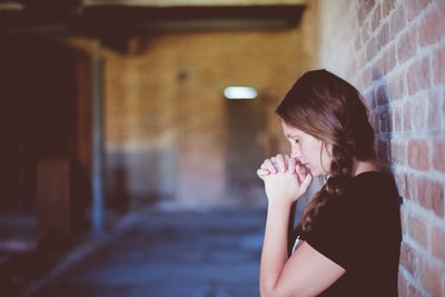 女人靠在砖墙上祈祷
